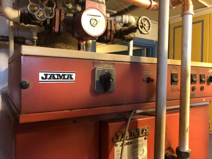 Röd, finsk panna märkt "JÄMÄ" med påkopplad cirkulationspump och shunt, okänd låda överst med blinkande LED-lampor.