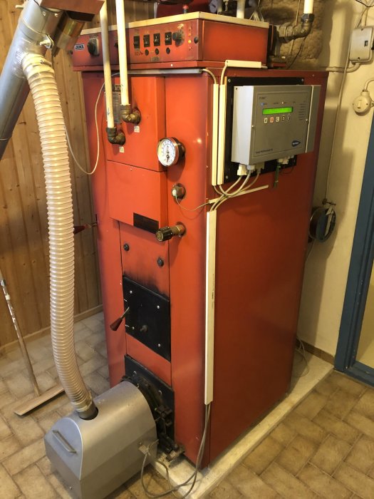En röd oljepanna konverterad till pellets med instruktioner på finska, LED-styrlåda och separat shunt.