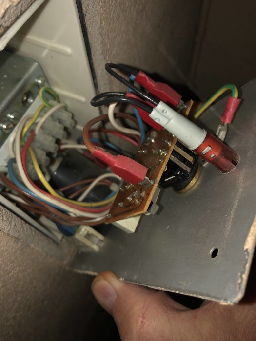 Närbild av inre elektronik till en fläktstyrpanel med synliga ledningar och komponenter, skadad termostat förevisad.