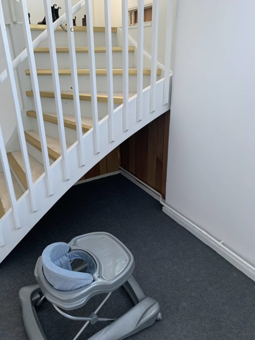 En trapp och ett barnstolsunderrede på mörk heltäckningsmatta, vilket illustrerar källargolvet där kaminen kan placeras.