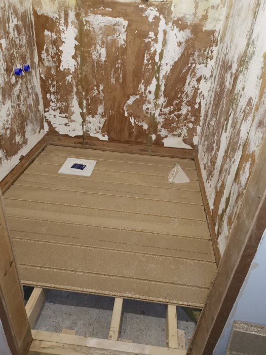 Outrivet badrum med nytt golvspån och väntande installation av golvvärme och isolering.