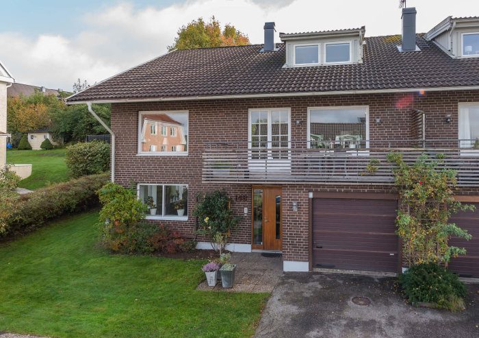 Parhus med brun tegelfasad, mörkbrunt tak och vit med brun kombination på första våningens fasad samt garageport.