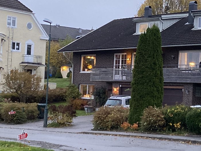 Ett parhus i skymningen med brun tegelfasad, vita fönster och en bil parkerad framför.