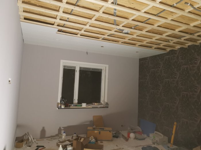 Renoveringsprojekt av rum med oavslutad takinstallation, verktyg och material utspritt på golvet.