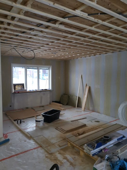 Rum under renovering med träreglar i taket och byggmaterial på golvet.