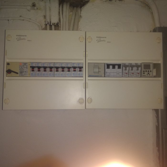 Två elcentraler på en vägg med flera säkringar, en av brytarna utlöst.
