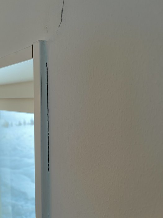 Sprickor längs kanten av ett fönsterkarm i en vitmålad vägg inomhus.