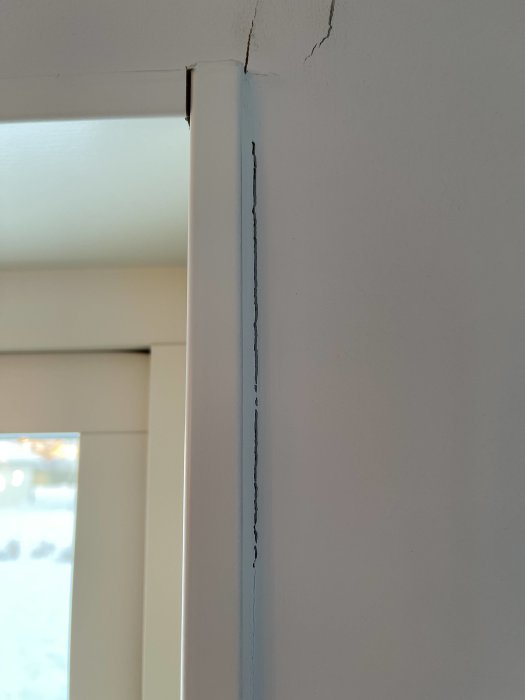 Vertikal spricka längs en dörrkarms hörn i ett ljust rum.