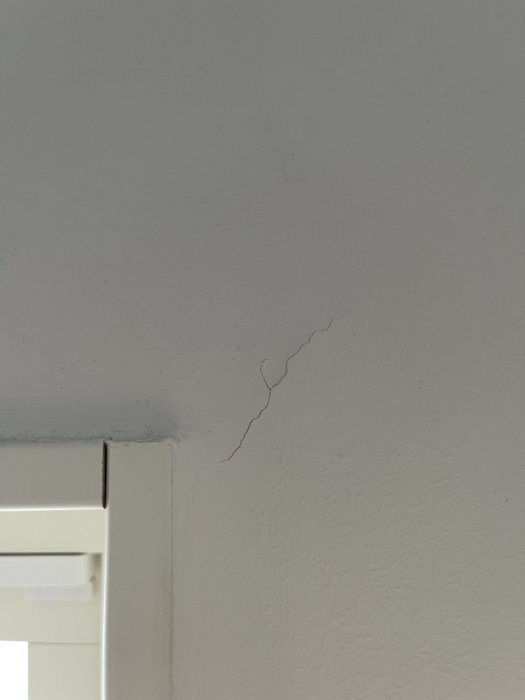 Spricka i en vitmålad vägghörn och tak i ett nytt hus, vid en dörrkarm.