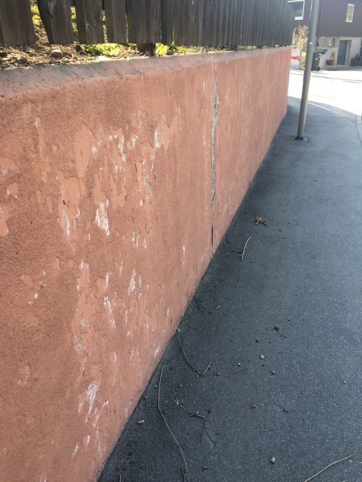 Mur med skadad puts och synliga sprickor och hål längs en trottoar.