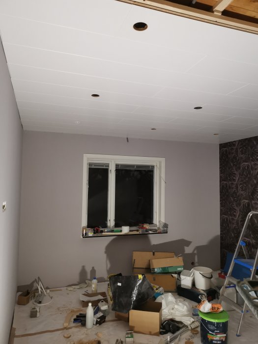 Installation av vitt tak i sovrum med osatta paneler och byggmaterial på golvet.