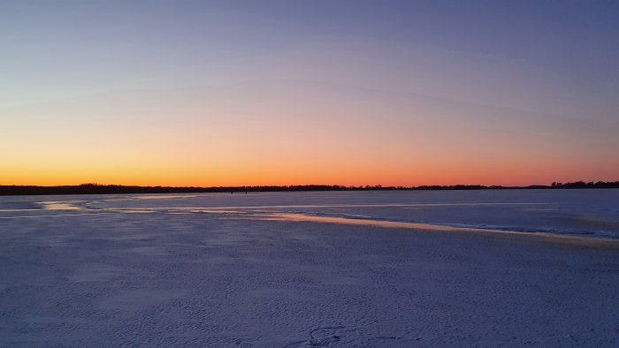 Solnedgång över en frusen sjö med snö och is under en klar himmel.