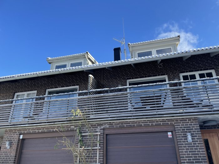 Tvåvåningshus med mörka tegelfasader och grå garageportar under en blå himmel.