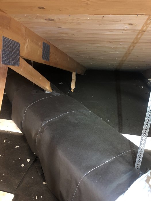 Vindpapp och isolering på vind med synliga takstolar och ventilationsslangar.