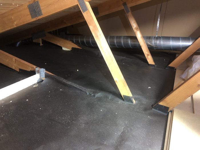 Kallvind med nyinstallerade ventilationsslangar, vindpapp och trästöd på en bostadsisolering.