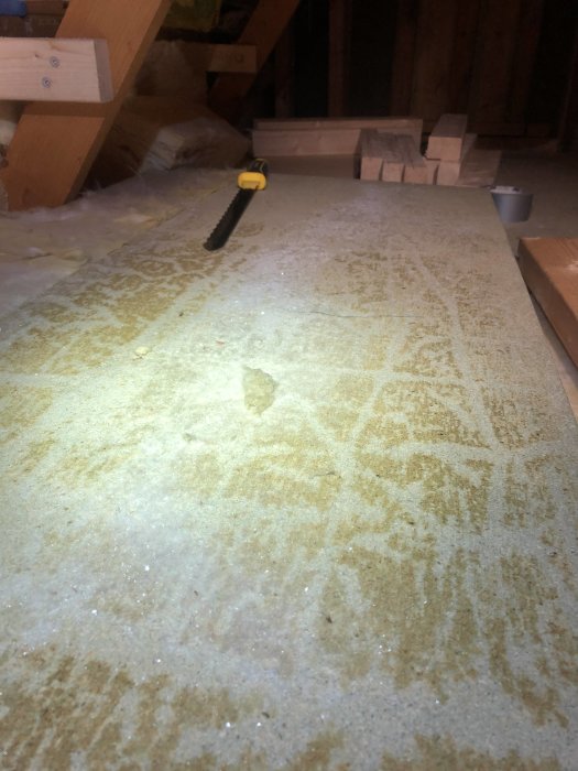 Isolering i vindsutrymme med spånskiva fryst fast, synligt frost och verktyg.