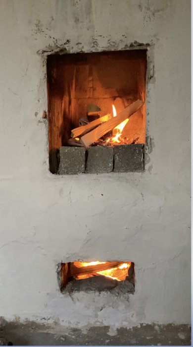 Eld brinner inne i en rörspisens eldkammare med en strategiskt placerad tegelsten, vilket indikerar en metod för att reglera draget.