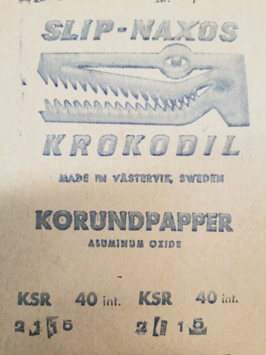 Logotyp för "SLIP-NAXOS KROKODIL" med en stiliserad krokodil, beteckningar för korundpapper och "Made in Västervik Sweden".