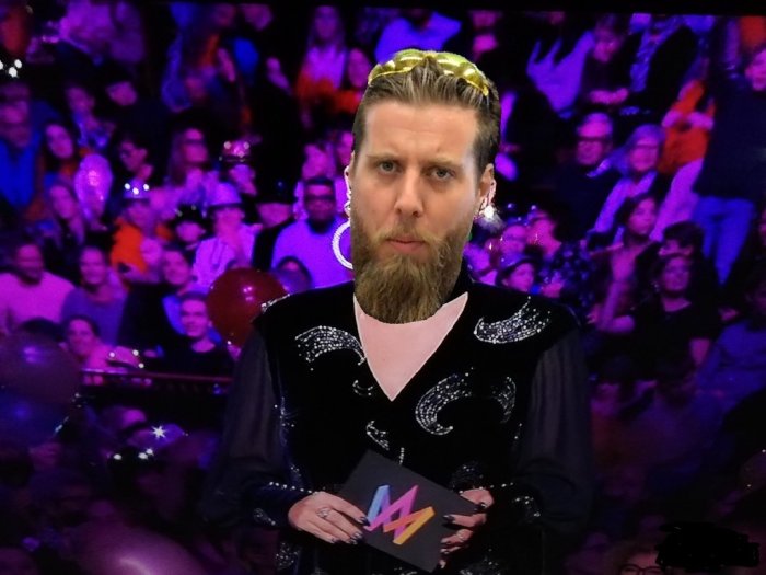 Man i glitterjacka med mikrofon står framför publik, scen från Melodifestivalen.