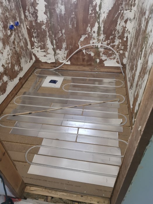 Utrullad golvvärme och plåtar på ett bjälklag med vägganslutning i ett renoveringsprojekt.