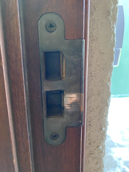 Befintligt slutbleck i en dörrkant, avsedd för ett låshus, med synlig skruv och skåra där låset går in.