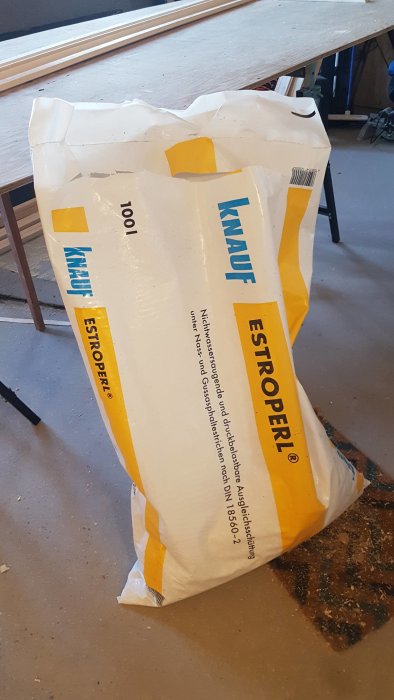 En säck med Knauf Estrich-Estroperl på ett byggarbetsgolv med sågspån runtomkring.