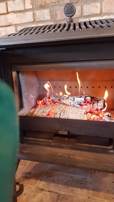 Brinnande och förkolnad ved i en öppen braskamin.