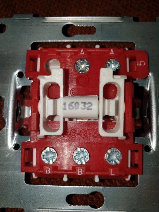 Närbild av en Elko strömbrytare monteringsdel med märkningen 'B' och 'L' utan sinusvågsymbol.