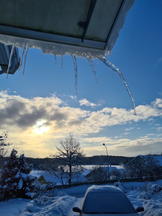 Vinterlandskap med isformationer på takkanten, solnedgång och snötäckt bil i förgrunden.