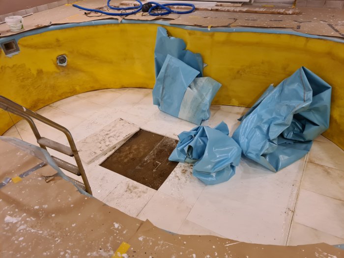 Renoveringsarbete på en inomhuspool, synlig pooltrappa och gammal blå poolduk samlad på sidan.