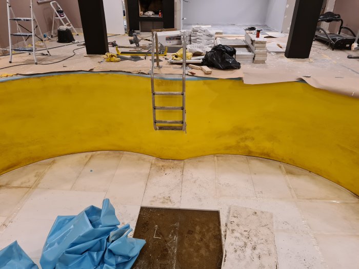 Tom inomhuspool under renovering med avlägsnad poolduk, synlig betong och byggmaterial runtomkring.