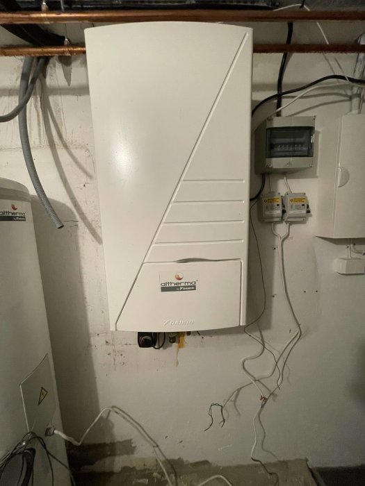 Daikin Altherma värmepump monterad på vägg i källare, kablar och rör synliga, intill elmätare och säkerhetsbrytare.