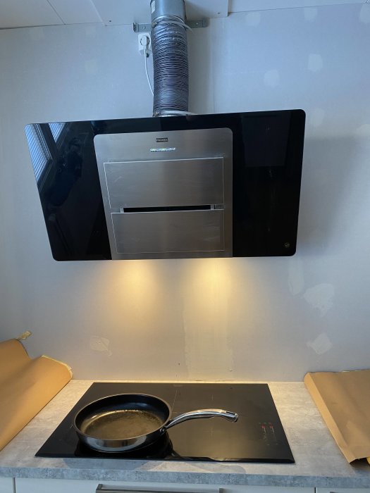 Kök under renovering med en nyligen installerad vägghängd fläkt och spacklade väggar.