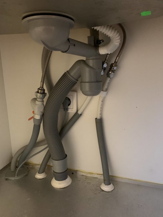Uppkoppling av avloppsrör och slangar under vask kopplat till diskmaskin.