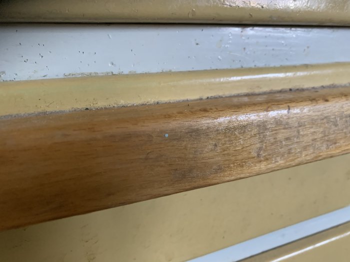 Närbild på ett långt, slitet handtag i bok på en äldre kökslåda med tydliga användningsspår.