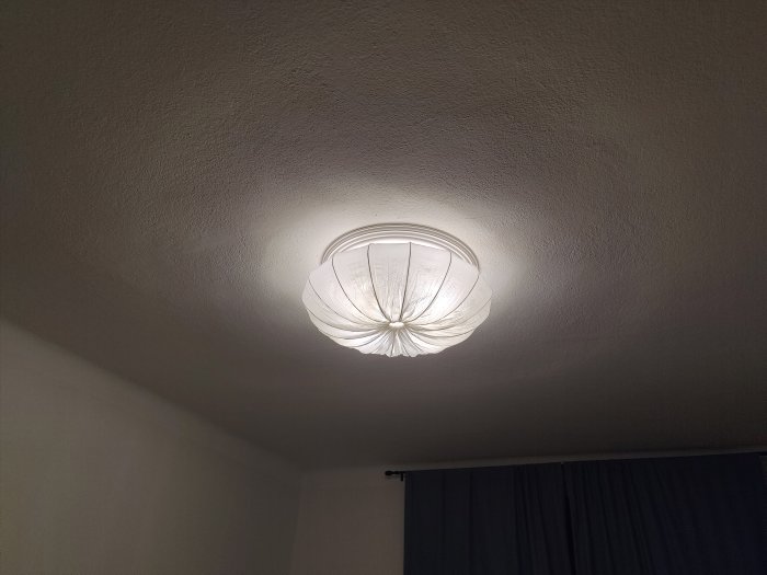 Taklampa med diffuser ger ett blaskigt ljus mot en vit takyta i ett sovrum.