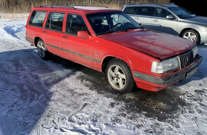 Röd herrgårdsvagn parkerad på isig yta med snö, närbild där fokus är på snö och is omkring fordonet.