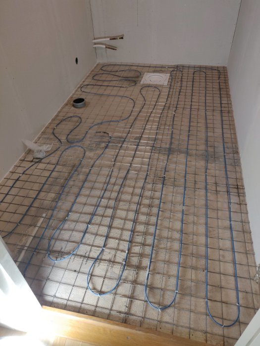 Ombyggt golv med nyinstallerad armering och utlagd golvvärmekabel i slingor på träunderlag.