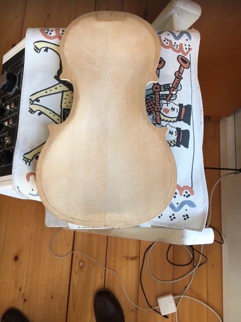Gitarrlock på ett broderat tyg ovanpå en högtalare med experimenteringsutrustning och laddare på ett trägolv.