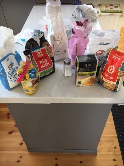 Öppna förpackningar av socker, rågmjöl och andra bakvaror utspridda på ett köksbord.