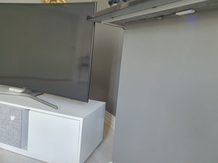 Tv-apparat ovanpå en vit mediabänk med dold teknikutrustning och en vit fuskvägg för hemautomationssystem.