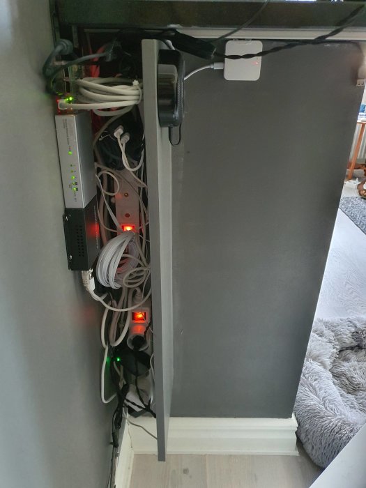 Trångt utrymme bakom en TV möblerar med kabeltrassel, en Raspberry Pi med SSD, förlängare för USB-sticka, hubs och adaptor.