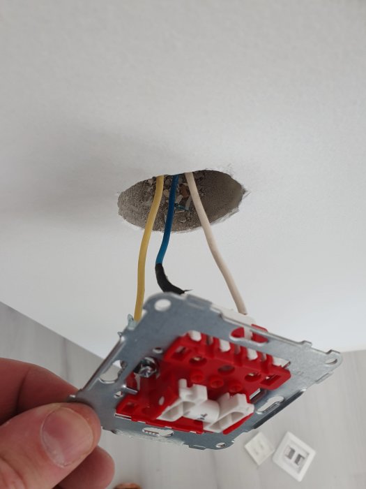 En hand håller en äldre strömställare med vita, gula, svarta och blåa kablar i ett tak.