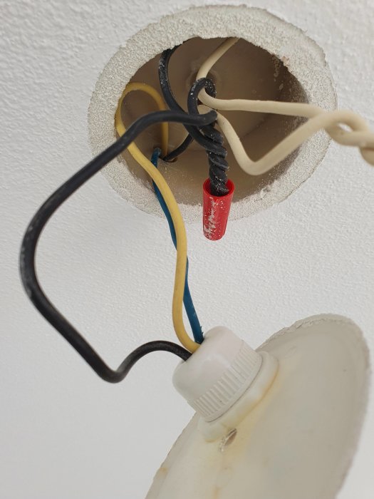 Äldre strömställare med vit, gul, svart och blå kabel exponerad vid installation.