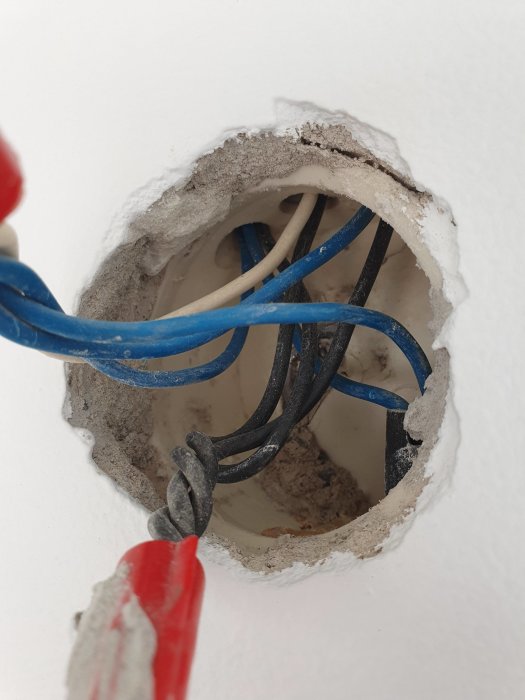 Öppen elektrisk väggdosa med en vit, gul, svart och blå kabel som är synliga, indikerande ett pågående arbete med elinstallation.