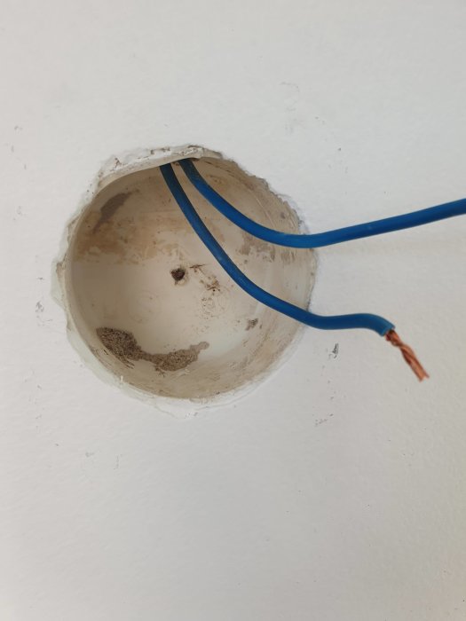 Öppet eluttag i vägg med vit, gul och blå kabel, där den blå kabeln är frilagd.