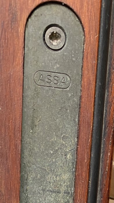 Närbild på en dörrstolpe med en sönderborrad skruvskalle märkt "ASSA" och glipa vid vredets position.