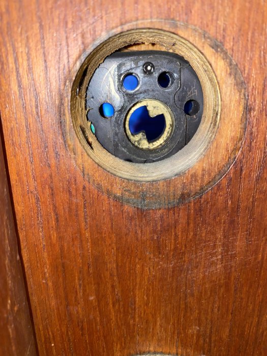 Nerbult dörrhandtagshål med en synlig skadad skruvskalle och en glimt av låshuset i en träfärgad dörr.
