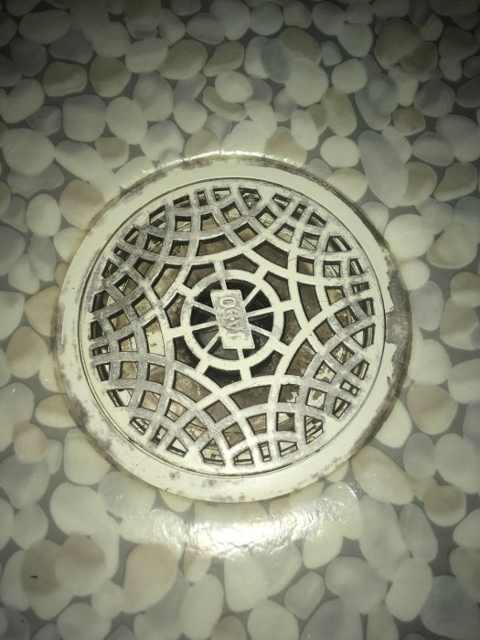 Golvbrunn omgiven av vita stenar med mörka fläckar på dess vita galler.