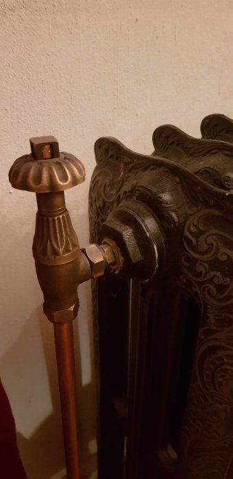 Detalj av en gammaldags radiator med utsmyckade mönster och en kopplad termostatventil.